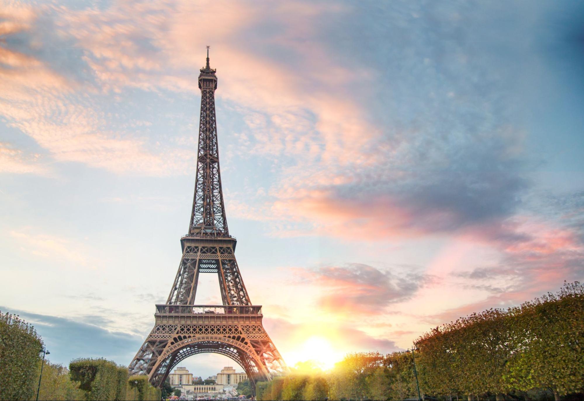 View on Eiffel tower through green summer trees with sunset rays